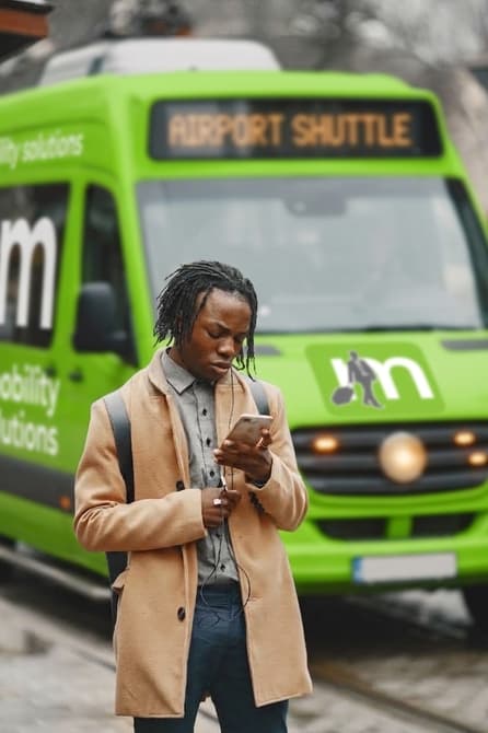 A passenger checking the Msafiri app on his phone in front of a branded airport shuttle